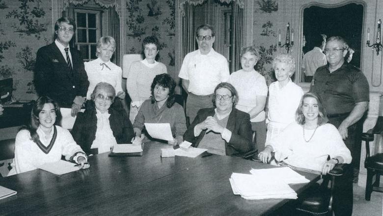 A black-and-white photo of a group of people around a table.